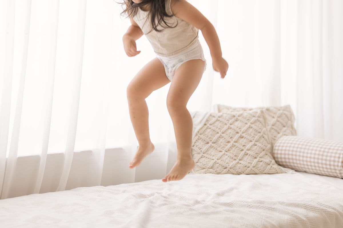 A toddler jumping on the bed in Little Rei pull-up pants