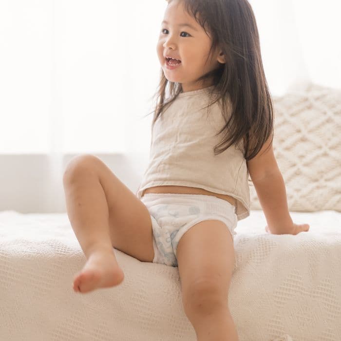 A toddler climbing onto the sofa in Little Rei pull-up pants