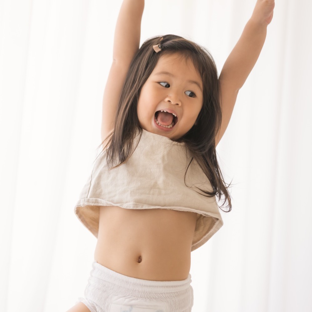 A toddler throwing their arms up with joy in Little Rei pull-up pants